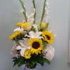 Tall bouquet of sunflowers, white lilies, and yellow roses in a glass vase