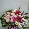 Pink roses and magenta lilies arranged in a pink hatbox