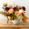 Mixed bouquet of peach, burgundy, and cream flowers in a white vase