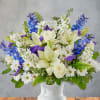 White lilies, roses, daisies, and blue flowers in a white vase