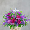 Purple and pink floral arrangement with a clear cross topper in a pedestal vase