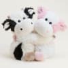 Two plush cow toys, one black-and-white and one pink-and-white, sitting together
