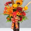 Orange and red mixed flower arrangement in a dark vase with a patterned ribbon