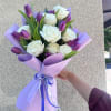 White roses and purple tulips are arranged in a rounded hand-tied bouquet