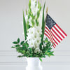 White gladiolus arrangement in a white urn with an American flag