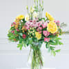 Mixed bouquet of yellow roses, pink blooms, and white flowers in a glass vase