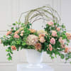 Pastel floral arrangement in a white pedestal vase with an arched twig frame