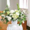 White floral arrangement in a white vase with green accents