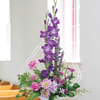 Purple and pink floral arrangement in a white vase with a decorative arch