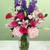 Pink roses and lilies in a glass vase with tall purple blooms