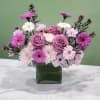 Pink and lavender roses with daisy-like flowers in a square glass vase