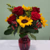 Bouquet of red roses and yellow sunflowers in a red glass vase