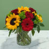 Bouquet of sunflowers, red roses, and a red gerbera daisy in a glass vase
