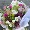 Hand-tied bouquet of pink, white, and purple flowers wrapped in white paper