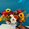 Colorful bouquet with sunflowers, roses, and orange blooms in a white vase