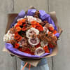 Bouquet of orange and blush roses wrapped in purple paper
