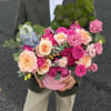 Pink and peach roses arranged in a round pink box with blue blooms