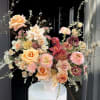 Large floral arrangement with peach, pink, and burgundy blooms in a white vase