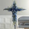 Blue and white floral cross-shaped funeral spray on an easel