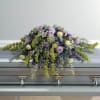 Pastel floral casket spray with purple, yellow, and white blooms