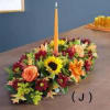 Low floral centerpiece with a tall orange taper candle