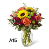 Mixed bouquet of orange roses, yellow sunflower, and magenta flowers in a glass vase