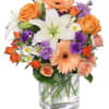 Mixed bouquet of orange, white, and purple flowers in a glass vase