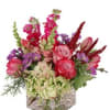 Mixed bouquet of pink, red, and purple flowers in a square glass vase