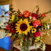 Rustic arrangement of sunflowers, red and orange roses, and daisies in a wood-textured vase