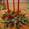 Low evergreen centerpiece with red roses and berries around three tall red taper candles