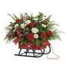 Red and white floral arrangement with evergreens and pinecones in a red sleigh container