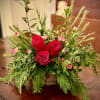 Low basket arrangement of red roses and small pink flowers with abundant evergreen foliage