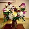 Mixed bouquet of roses, carnations, and white spider mums in a tinted glass vase with red berries