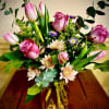 Pink roses, tulips, and pale peach mums with purple accents in an amber glass vase.