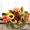 Low rectangular arrangement of sunflowers, orange roses, orchids, and berries in a clear glass vase.