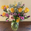 Mixed bouquet of yellow roses, pink roses, purple tulips, and small white daisies in a clear glass vase