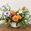 Mixed bouquet of orange roses, tulips, and pastel flowers in a white vase