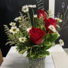 Red roses and white daisies in a glass jar with greenery