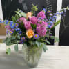 Mixed bouquet of pink, peach, and blue flowers in a glass vase