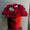 Red roses arranged in a round red hat box with a ribbon