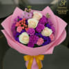 Pink-wrapped bouquet of cream roses, purple blooms, and pink accents with a yellow ribbon