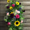 This large standing spray features sunflowers and multiple color in season flowers.