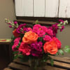 This arrangement has orange Roses, purple stock, hot pink spray roses, hot