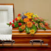 This graceful casket spray of bright blossoms in shades of red, orange