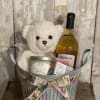 This basket of goodies includes a teddy bear, a bottle of wine