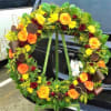 This wreath includes Orange bi-colored Roses, Red Spray Roses, Yellow Cushion Mums