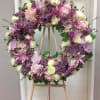 All lavender and purple shade flowers arranged on tall funeral stand.