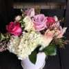 Hydrangeas, roses, sweet peas, dusty miller arranged in a white ceramic pot.