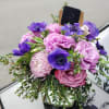 A modern Arrangement using light purple mums, true purple anemones and roses.