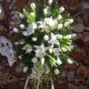 This funeral arrangement contains white roses and white lilies. 